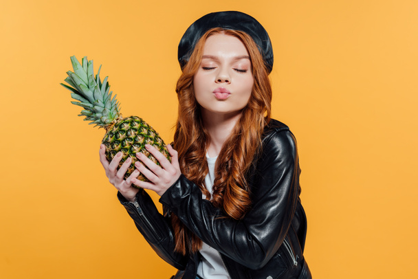 belle fille rousse en veste en cuir tenant l'ananas et les lèvres boudantes isolées sur jaune
 - Photo, image
