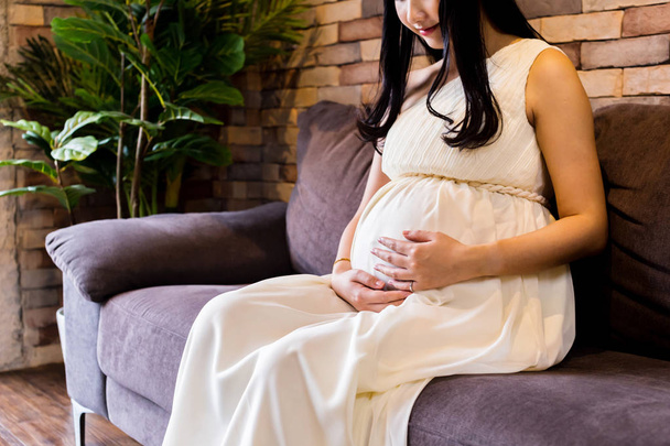 Mulher grávida tocando bebê dentro do estômago no sofá
 - Foto, Imagem