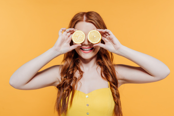 zrzovaná dívka zakrývající tvář citrony a usmívající se izolovaně na žluté - Fotografie, Obrázek