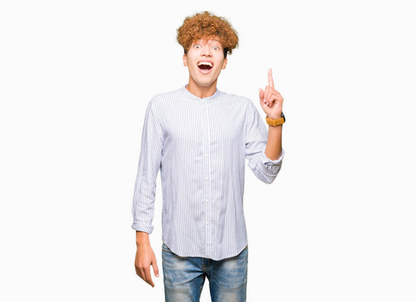 Young handsome business man with afro hair wearing elegant shirt pointing finger up with successful idea. Exited and happy. Number one. - 写真・画像