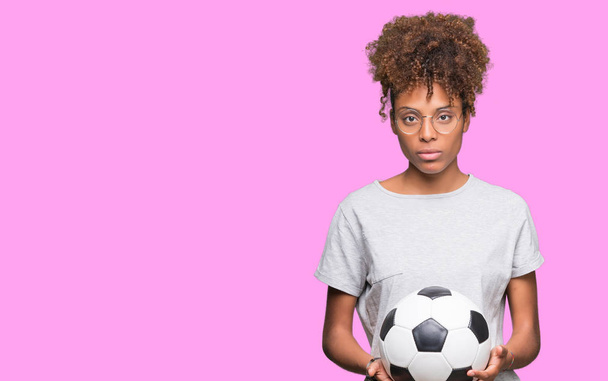 Mujer afroamericana joven sosteniendo pelota de fútbol sobre fondo aislado con una expresión de confianza en la cara inteligente pensando en serio
 - Foto, imagen