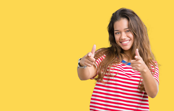 Jonge mooie brunette vrouw dragen strepen t-shirt over geïsoleerde achtergrond wijzen vingers naar camera met gelukkig en grappig gezicht. Goede energie en vibrafoon. - Foto, afbeelding