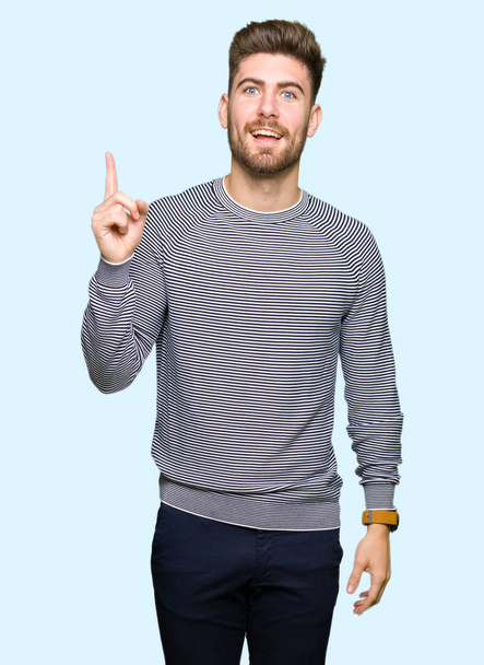 Молодий красивий чоловік у светрі, який вказує пальцем на успішну ідею. Вийшов і щасливий. Номер один
. - Фото, зображення