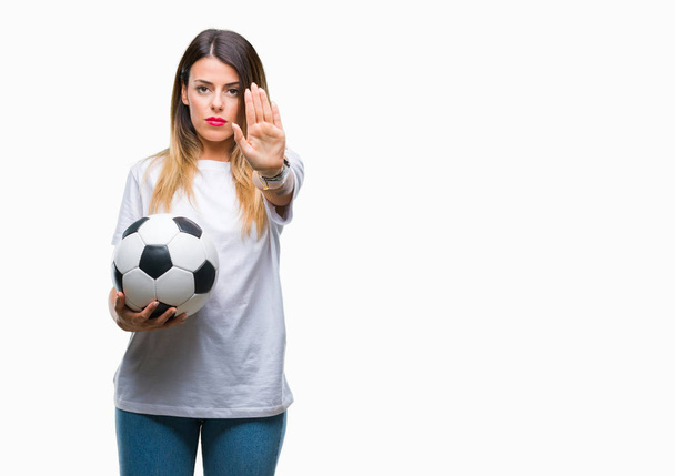 Молодая красивая женщина держит футбольный мяч на изолированном фоне с открытой рукой делает знак стоп с серьезным и уверенным выражением, защитный жест
 - Фото, изображение