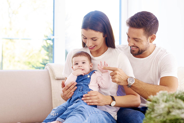 Happy young family sitting on sofa with their baby girl and havi - Foto, imagen
