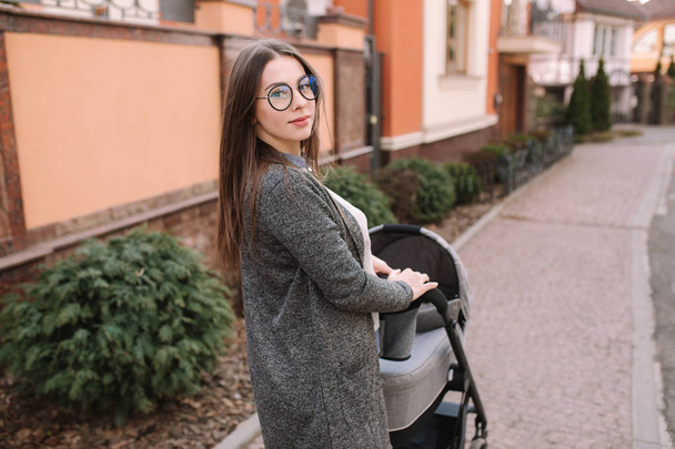 Attractive young mother walking with her little baby. Mom with newborn baby in pram - Photo, Image