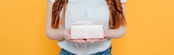 panoramic shot of girl in white t-shirt holding gift box isolated on yellow - Foto, imagen