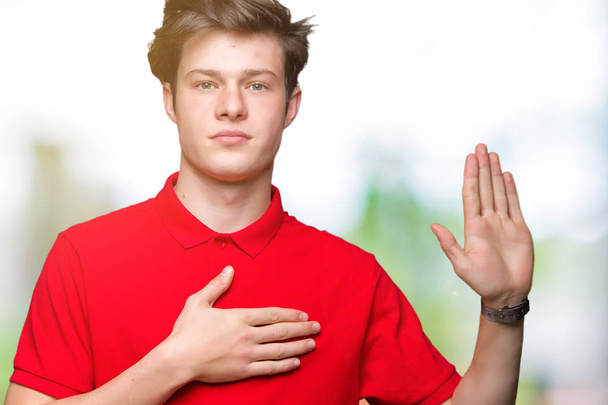 junger gutaussehender Mann mit rotem T-Shirt vor isoliertem Hintergrund, der mit der Hand auf der Brust und offener Handfläche flucht und einen Treueschwur leistet - Foto, Bild