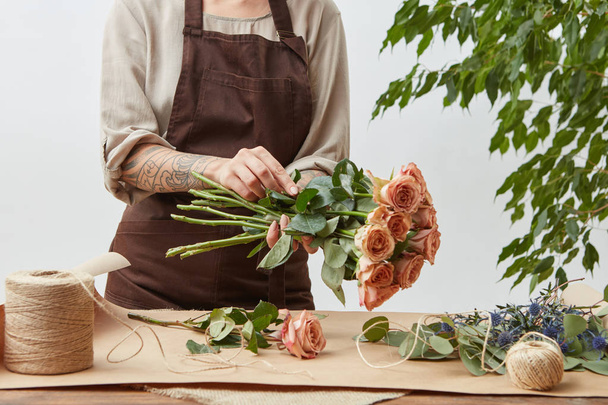 Girl florist is decorating beautiful bouquet from fresh natural roses step by step at the table with paper and rope on it. Mother's Day holiday. - Photo, image