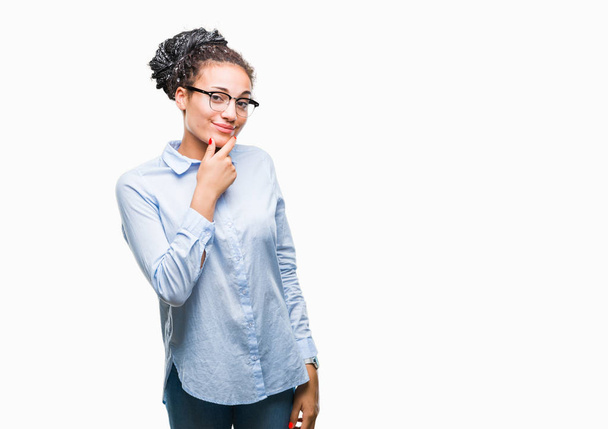 Jovem trançado cabelo afro-americano menina de negócios vestindo óculos sobre fundo isolado olhando confiante para a câmera com sorriso com braços cruzados e mão levantada no queixo. Pensar positivo
. - Foto, Imagem