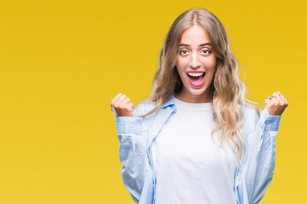 Beautiful young blonde woman over isolated background celebrating surprised and amazed for success with arms raised and open eyes. Winner concept. - Photo, image