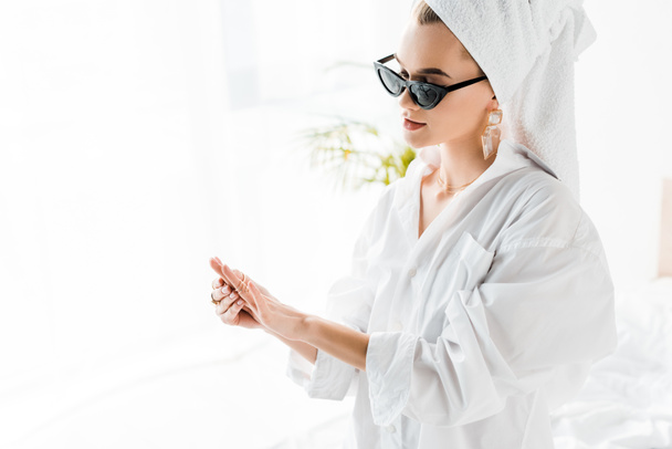 young stylish woman in shirt, sunglasses, jewelry and with towel on head looking at hand - Фото, изображение