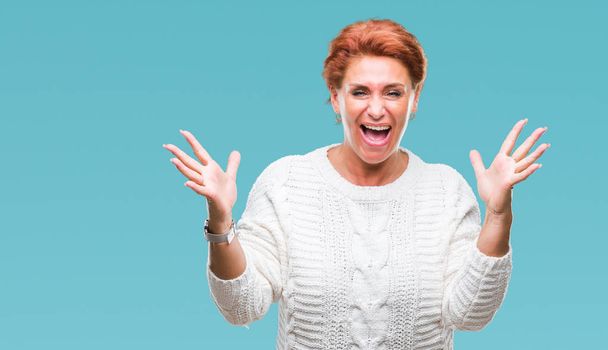 Atrractive senior caucasian redhead woman wearing winter sweater over isolated background celebrating crazy and amazed for success with arms raised and open eyes screaming excited. Winner concept - Fotoğraf, Görsel