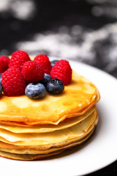 Closeup photo of plate of pancakes, blueberries, raspberries and powdered sugar. - Фото, зображення