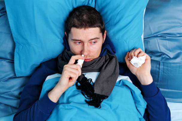 kranker brünetter Mann benutzt Nasenspray im Bett - Foto, Bild