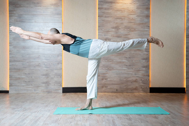Athletic man standing on leg with arms stretched forward doing yoga on blue mat . - Foto, Imagem