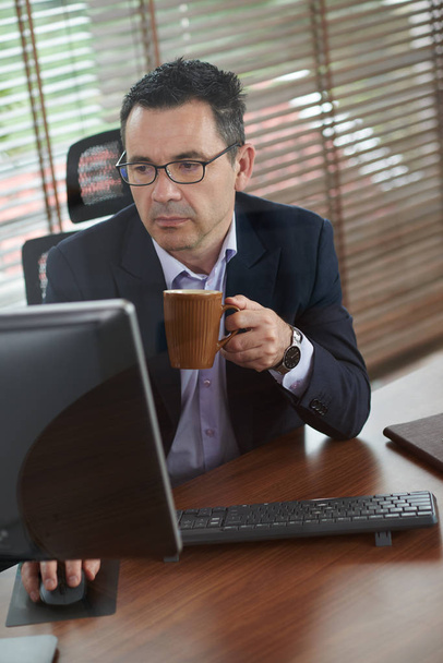 Ώριμος επιχειρηματίας πίνοντας πρωινό καφέ και απαντώντας σε e-mails - Φωτογραφία, εικόνα