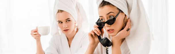 panoramic shot of stylish woman in bathrobe, sunglasses and jewelry with towel on head using retro telephone near woman with cup - 写真・画像