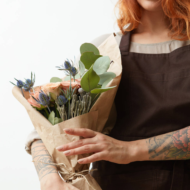 Wonderful summer fresh roses, eryngium and green leaves as a greeting bouquet in a female's hand with tattoo on a white background. Place for text. Gift for Mother's Day. - 写真・画像