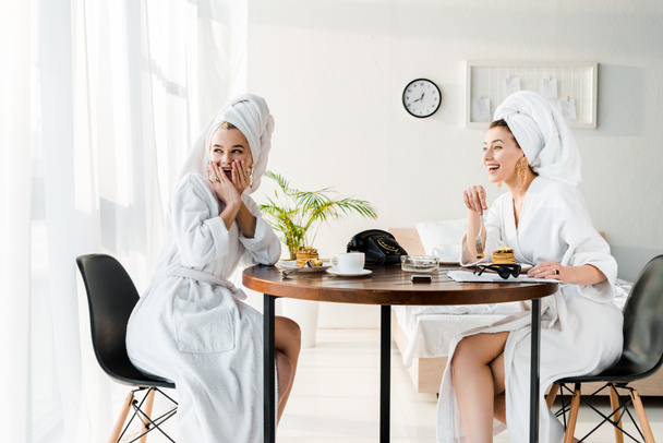 stylish happy and shocked women in bathrobes and jewelry with towels on heads having breakfast - Photo, Image