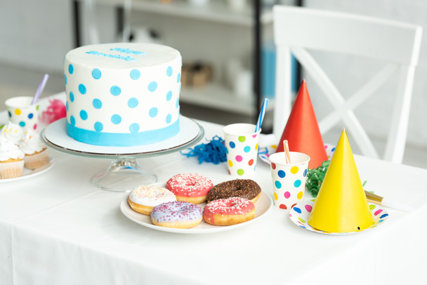 leckere Geburtstagstorte mit Cupcakes, Donuts und Pappbechern auf festlichem Tisch - Foto, Bild