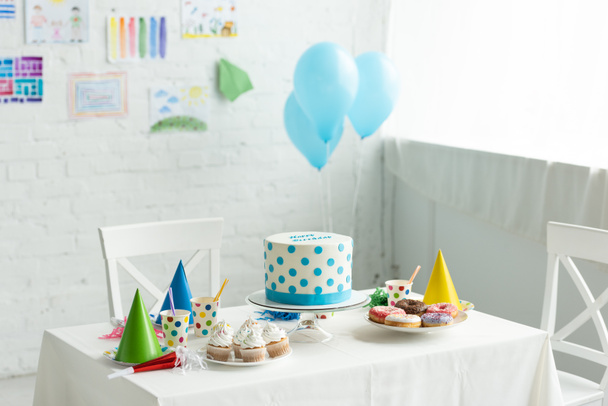 gâteau festif et casquettes de fête sur la table dans la chambre décorée pour la fête d'anniversaire avec des ballons à air
 - Photo, image