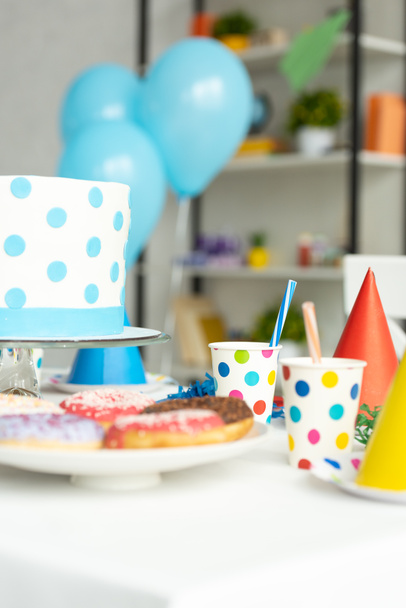 selectieve focus van verjaardagstaart, donuts en feest decoraties op tafel  - Foto, afbeelding