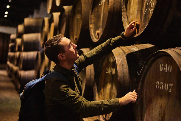 Молодой человек туристическая прогулка в старых старых деревянных бочках с вином в хранилище выстроились в прохладном и темном подвале в Италии, Порту, Португалия, Франция
 - Фото, изображение