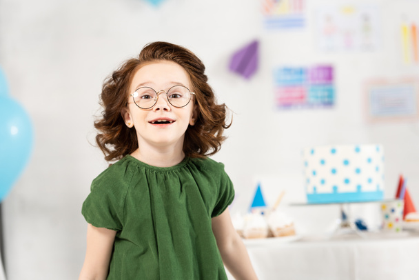 adorable kid in glasses looking at camera and smiling during birthday celebration at home - Foto, Imagen