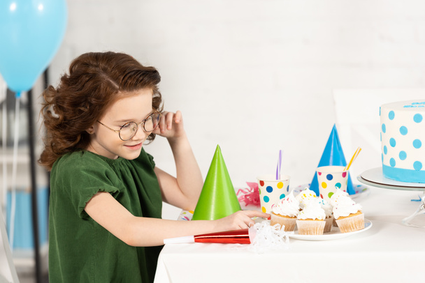 rozkošný kluk, co sedí u stolu s dortíky během narozeninového oslavy - Fotografie, Obrázek