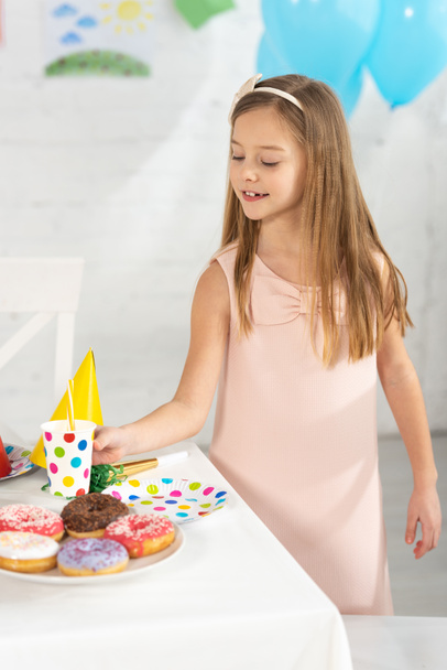adorable kid at birthday table with festive decorations and donuts during party - Photo, Image