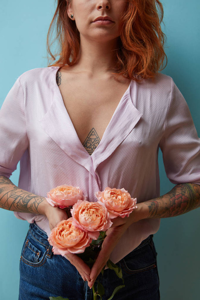 A bouquet of pink roses is holding in hands with tattoo a sexy red-haired girl around a blue background with copy space. Valentine's day concept - Φωτογραφία, εικόνα
