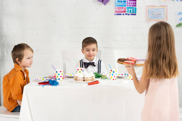 criança segurando prato com rosquinhas durante festa de aniversário com amigos em casa
 - Foto, Imagem