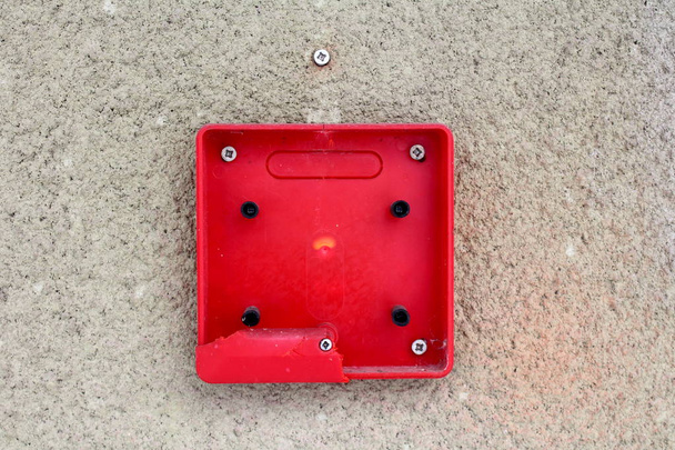 Całkowicie złamany czerwony alarm pożarowy plastikowy przełącznik zamontowany za pomocą wkrętów na zewnętrznej ścianie budynku - Zdjęcie, obraz