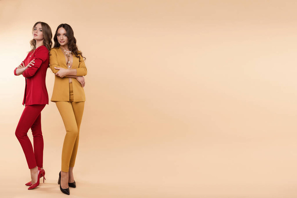 Two gorgeous models in colored suits and high heels over flat background. - Foto, Imagen