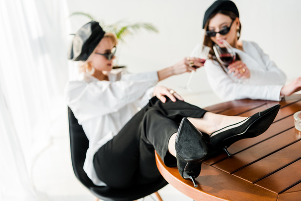 foyer sélectif de la femme élégante en béret noir et lunettes de soleil avec les jambes sur la table cliquetis avec un ami
  - Photo, image