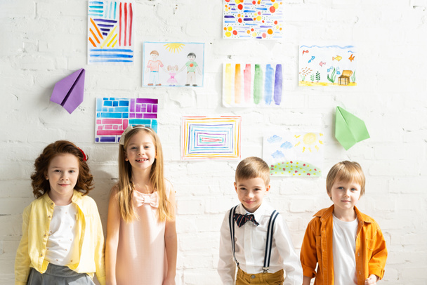 adorable kids posing and looking at camera near colorful paintings on wall at home - Fotoğraf, Görsel