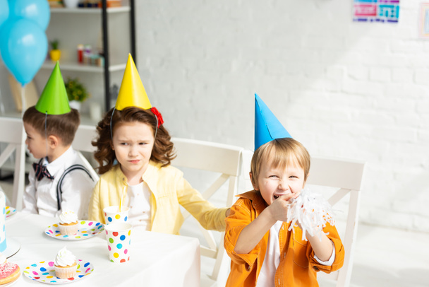 kids in party hats sitting at festive table during birthday celebration - Φωτογραφία, εικόνα