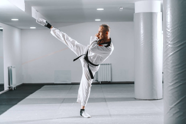 Caucasian trainer in dobok kicking with one leg in gym. Taekwondo class concept. - Photo, Image