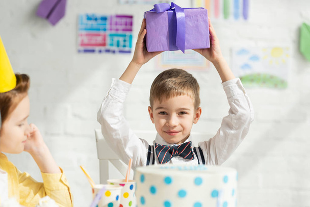 селективное внимание мальчика, держащего подарок и смотрящего в камеру во время празднования дня рождения
 - Фото, изображение