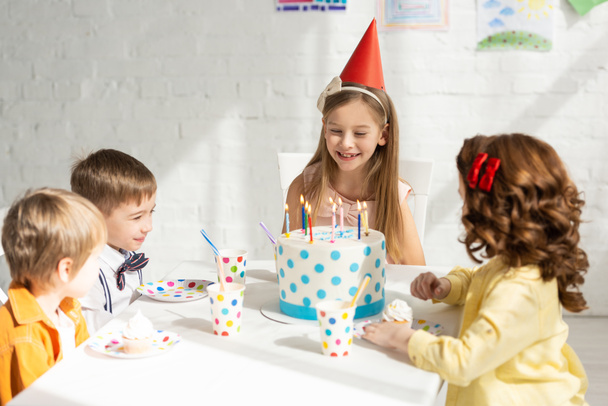 adorável crianças felizes sentadas na mesa de festa com bolo enquanto comemoram aniversário juntos
 - Foto, Imagem