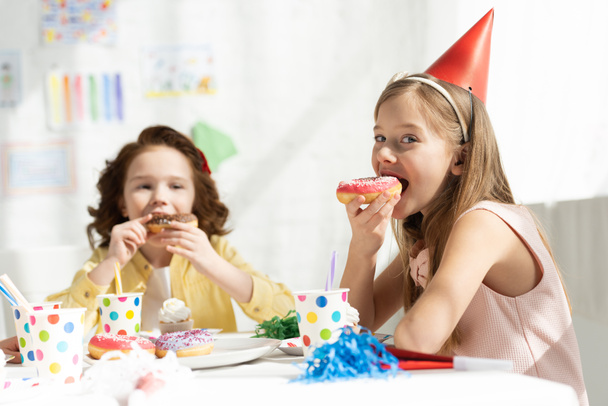 adorable kids sitting at party table and eating donuts during birthday celebration - Photo, Image