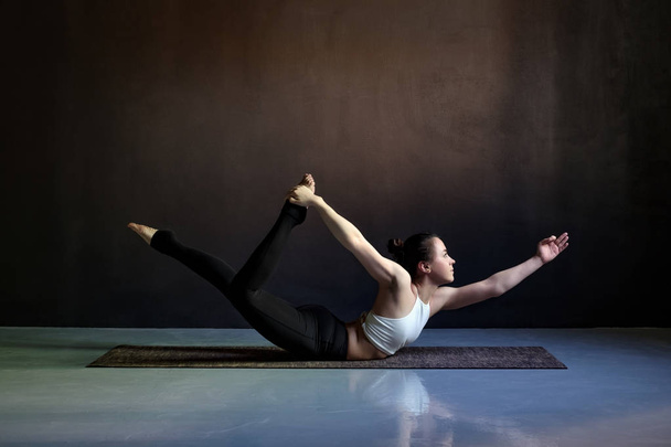 Jovem mulher atraente praticando ioga, alongamento em pose Salabhasana
 - Foto, Imagem