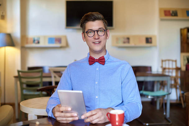 Portrait shot of young man wearing causal clothes while sitting at desk and using his digital tablet. Small business. - Photo, Image