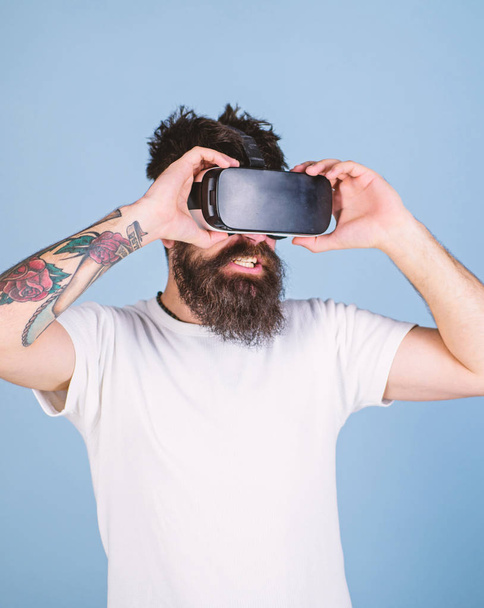 Man with long beard having cyber experience in VR glasses, digital innovations concept. Bearded man testing new device. Hipster with tattooed arm and stylish beard amused by 3D virtual reality video - Foto, imagen