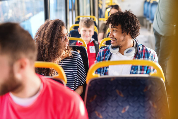 Νεαρό χαμογελαστό πολυπολιτισμικό ζευγάρι μιλάει ενώ κάθεται στο λεωφορείο της πόλης. - Φωτογραφία, εικόνα