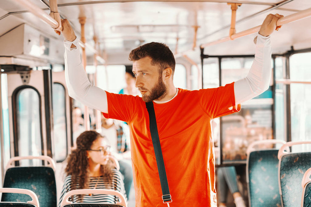Młody mężczyzna stojący w autobusie, trzymając do uchwytu, patrząc przez okno, myślenia. - Zdjęcie, obraz