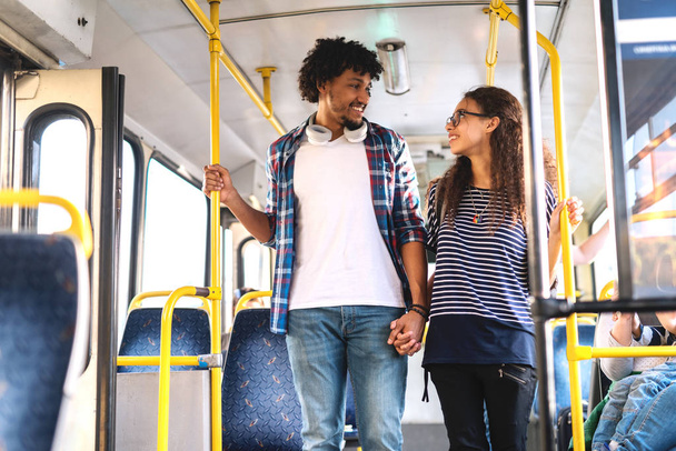Щаслива мультикультурна пара стоїть і тримає руки під час їзди на міському автобусі
. - Фото, зображення