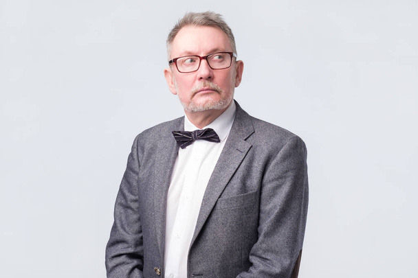 Senior businessman in jacket, glasses and tie looking up aside. - Фото, изображение