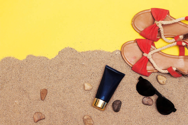 concepto de verano, sandalia de playa y tubo de crema azul y gafas de sol negras sobre arena con piedras
 - Foto, imagen